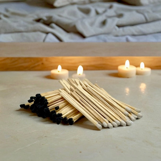 black and white tipped matches resting on countertop with lit tea candles in the background
